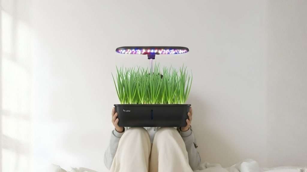 Here is a descriptive and SEO-friendly alt text for your blog post, designed to be clear for screen readers and search engines alike: Alt Text: A person sitting on the floor holding a LetPot indoor hydroponic garden system. The black planter is filled with a dense, lush harvest of tall green onions growing under a specialized LED grow light emitting a purple-tinted glow against a clean white wall.